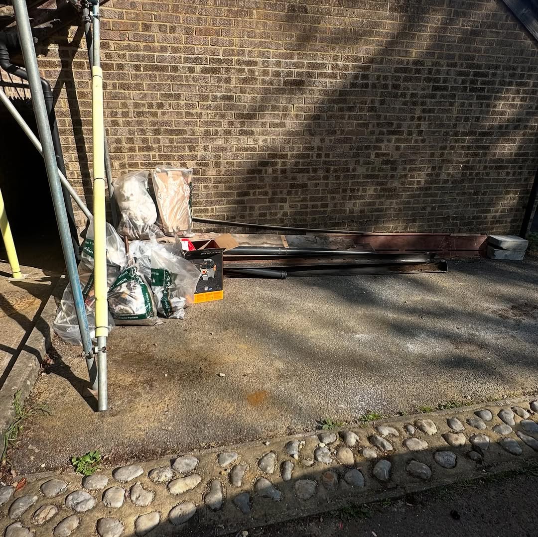 Builders waste and materials piled against a brick wall before clearance